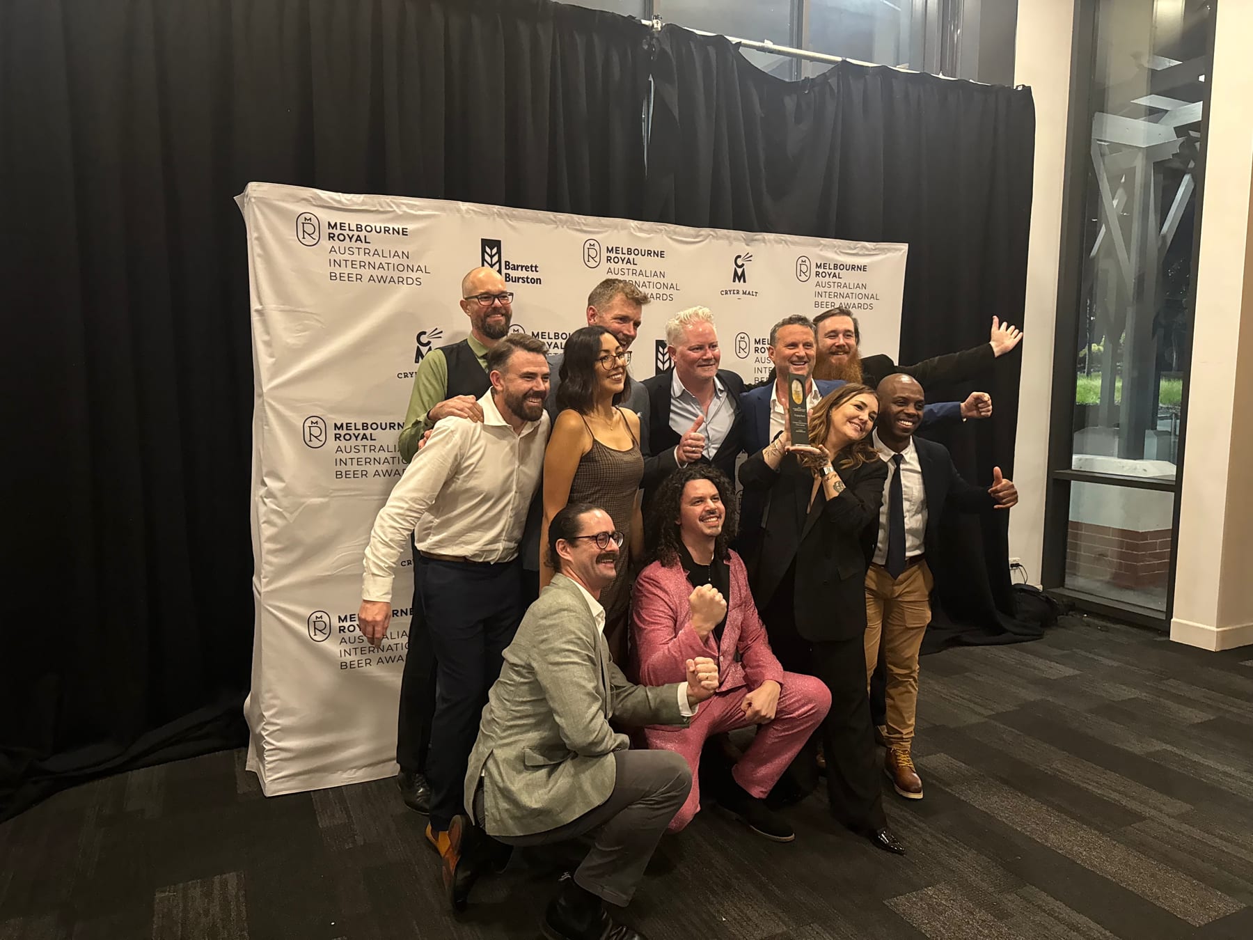 AIBA winners celebrating with a trophy in front of the Melbourne Royal Australian International Beer Awards backdrop