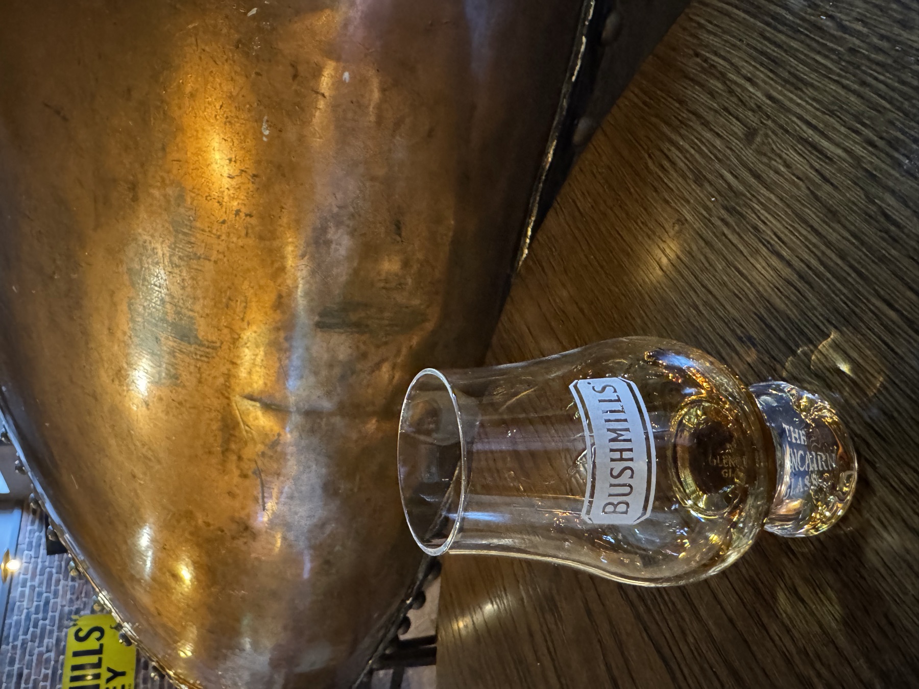 A Bushmills dram in front of a copper pot still